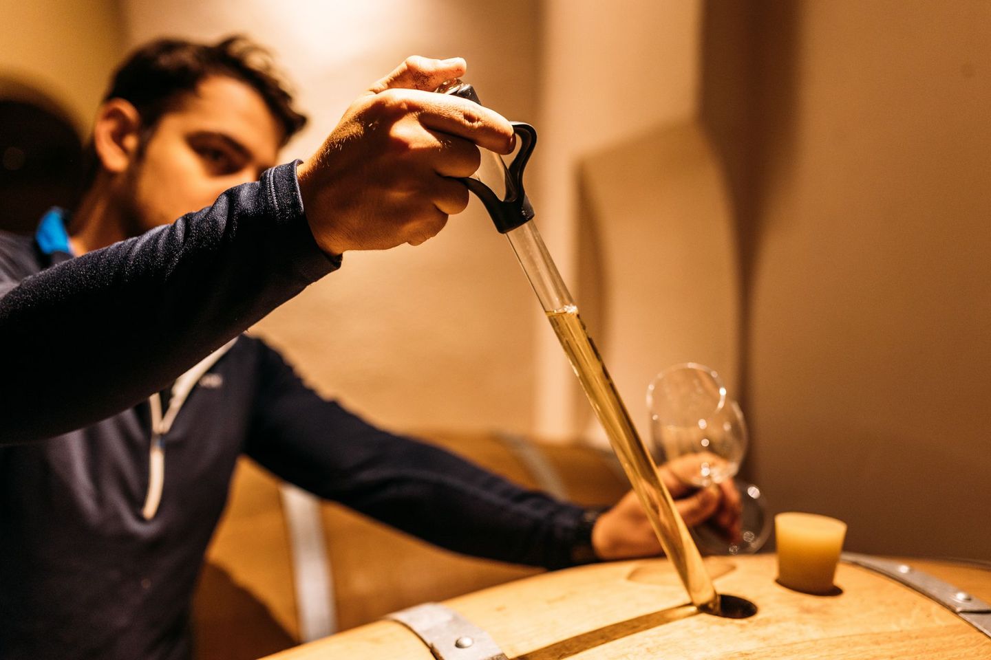 Un homme verse du vin dans un tonneau avec une pipette.