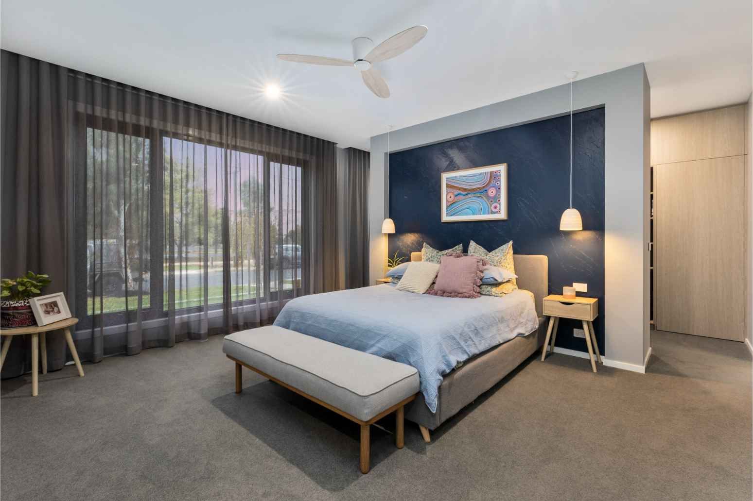 Modern Bedroom With a Blue Bedspread, Dark Accent Wall, and Large Windows With Curtains — Jetsonian Constructions In Wendouree, VIC