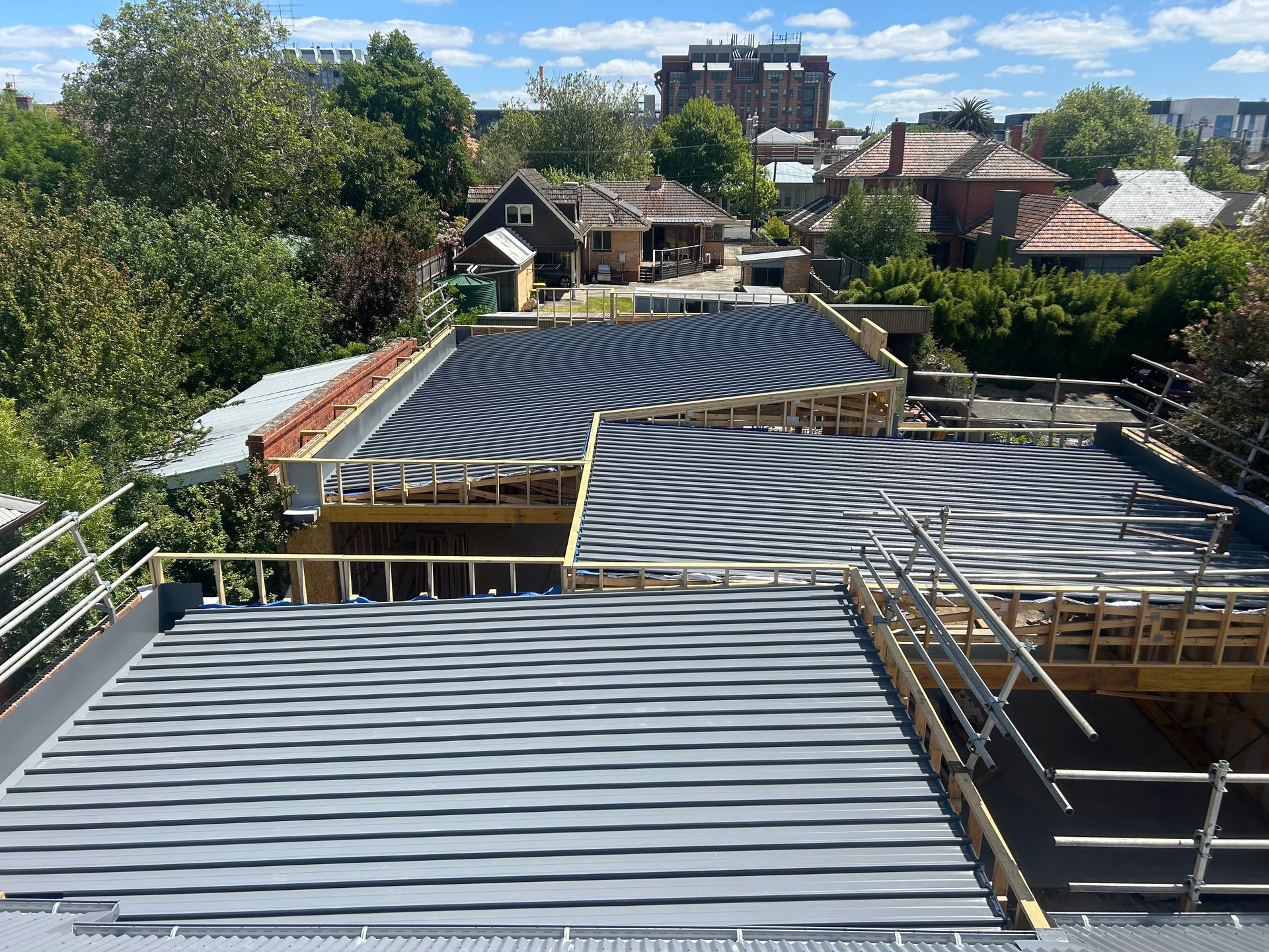 Rooftop Under Construction With Corrugated Metal Panels and Scaffolding Above Houses and Trees — Jetsonian Constructions In Wendouree, VIC