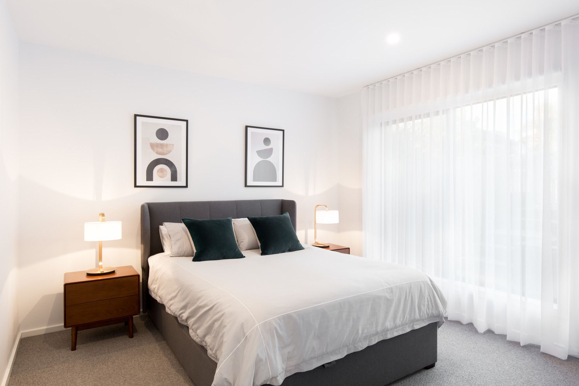Bright minimalist bedroom with a neatly made bed, two bedside lamps, framed art, and sheer curtains — Jetsonian Constructions In Wendouree, VIC