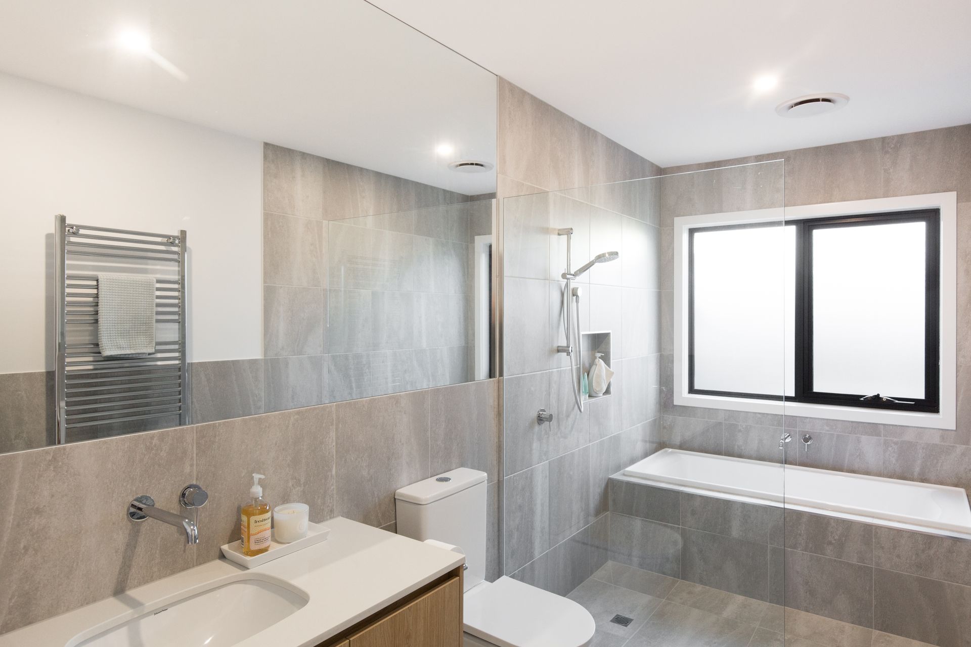 Modern bathroom with a sink, toilet, bathtub, shower, and large frosted window in gray tones — Jetsonian Constructions In Wendouree, VIC