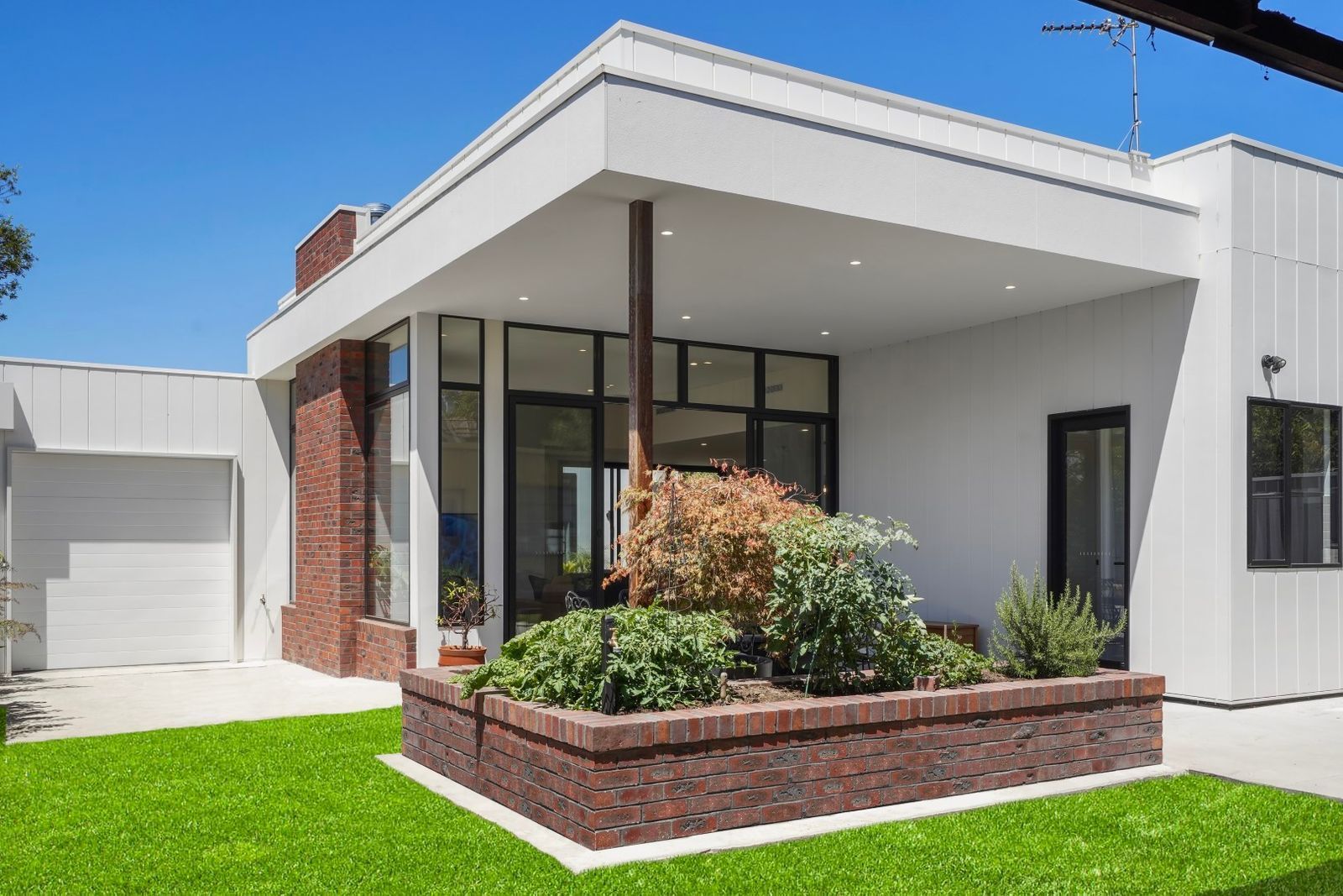 Modern White House With a Covered Porch, Brick Planter, and Green Lawn Under a Clear Blue Sky — Jetsonian Constructions In Wendouree, VIC