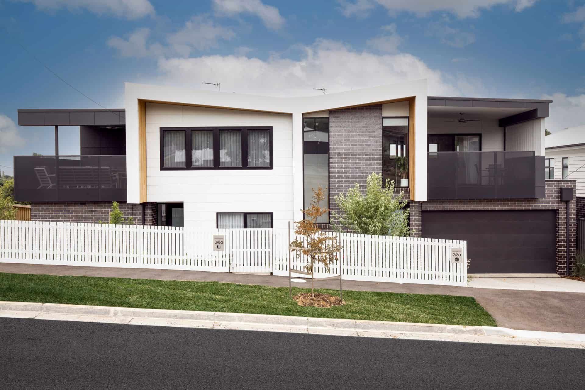Modern two-story house with white facade, black windows, and picket fence on a sunny day.