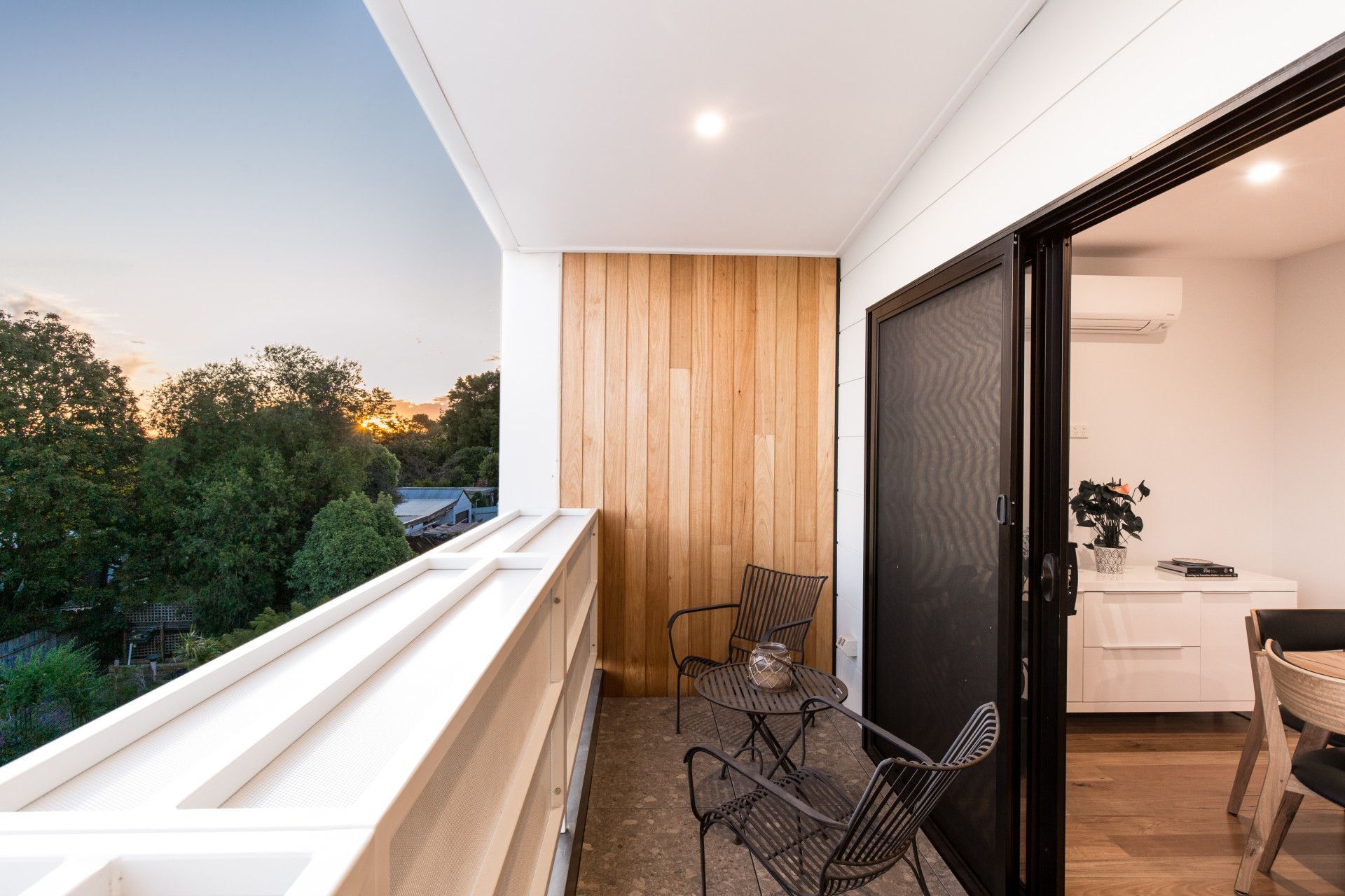Modern apartment balcony with chairs, wood paneling, and sliding doors overlooking trees at sunset — Jetsonian Constructions In Wendouree, VIC