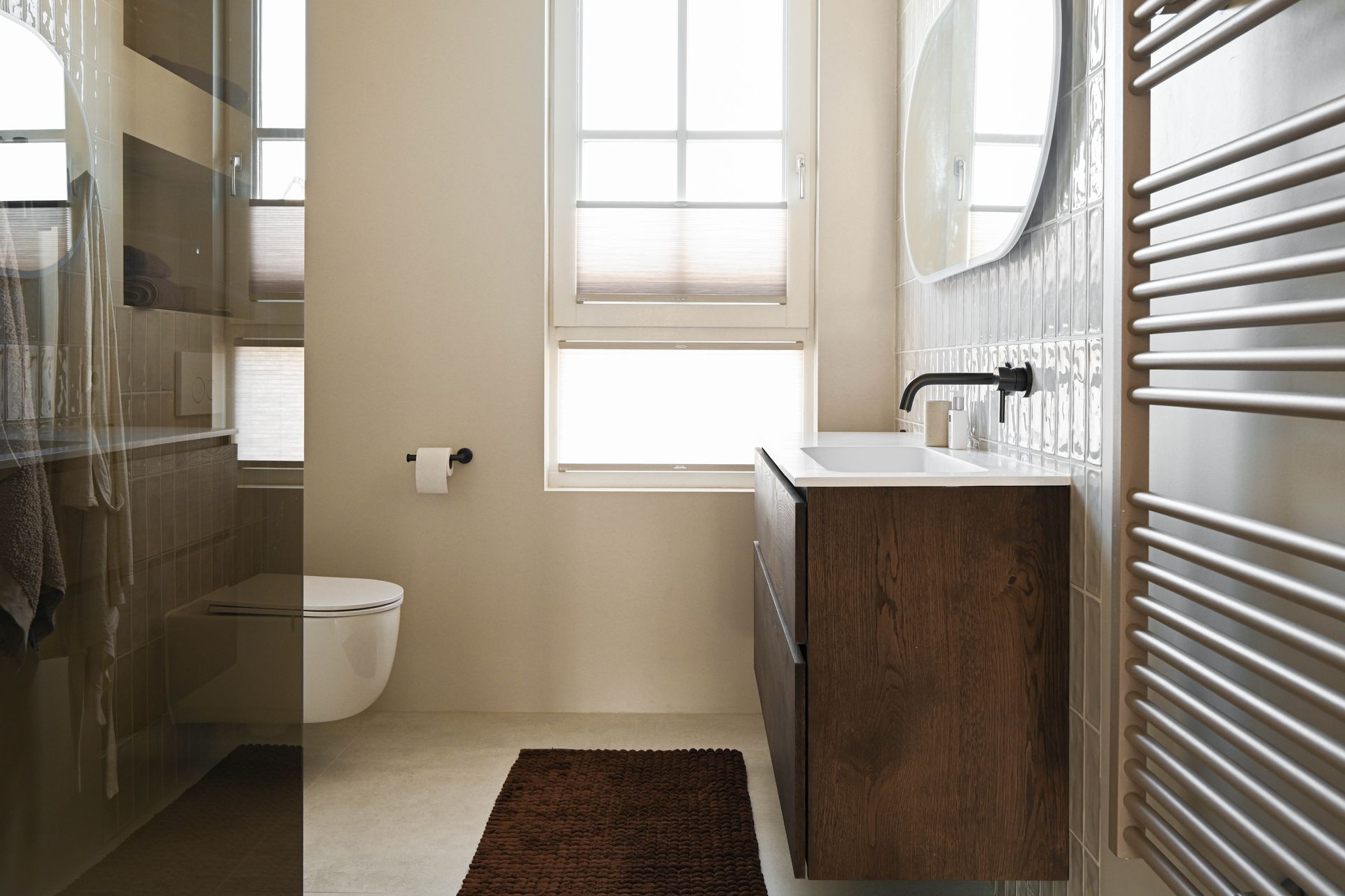 Badkamer met donkerhouten wastafelmeubel, wit toilet en raam met jaloezieën.