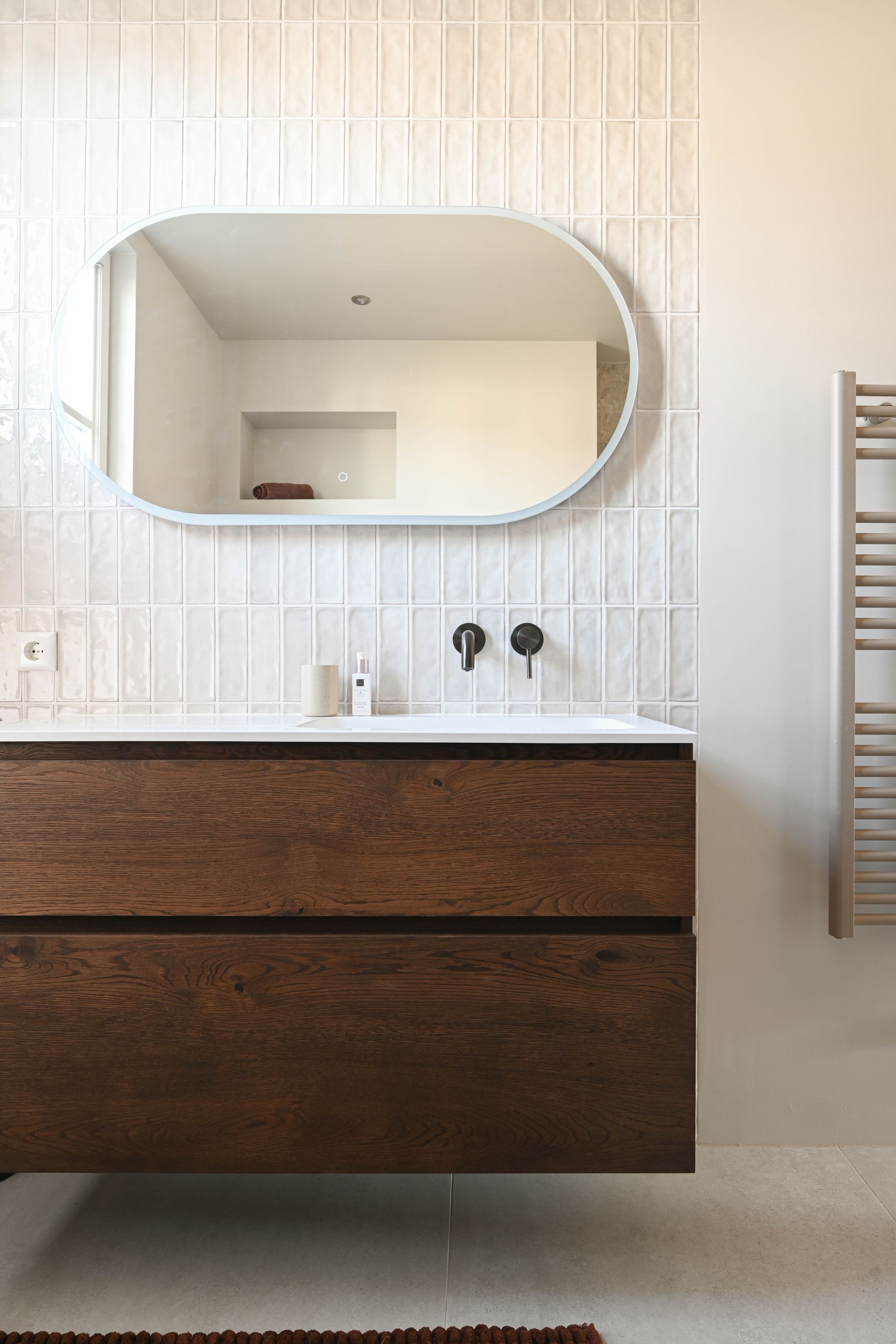 Moderne badkamer met zwevend houten badmeubel, ovale spiegel, witte tegels met structuur en zwarte kranen.