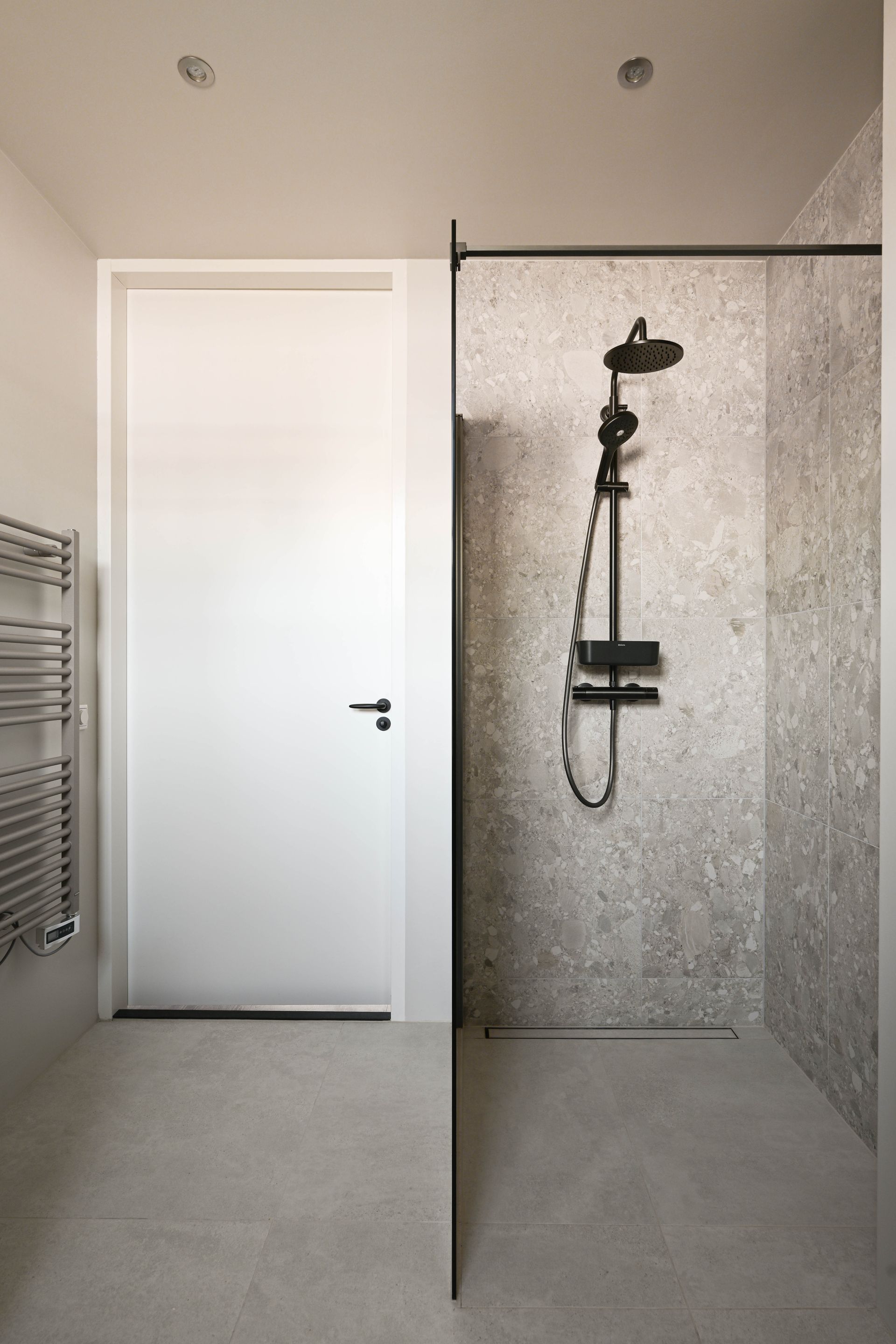 Moderne badkamer met inloopdouche. Witte deur, grijs gespikkelde muur en vloer, zwarte douchekranen.