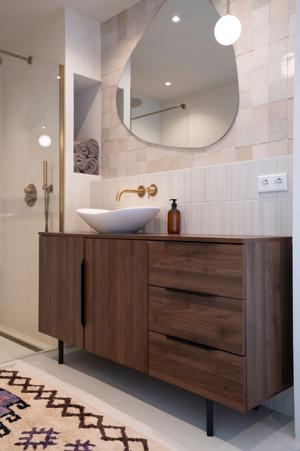 Moderne badkamer met een houten wastafelmeubel, een bijzondere spiegel en een kleurrijk vloerkleed.
