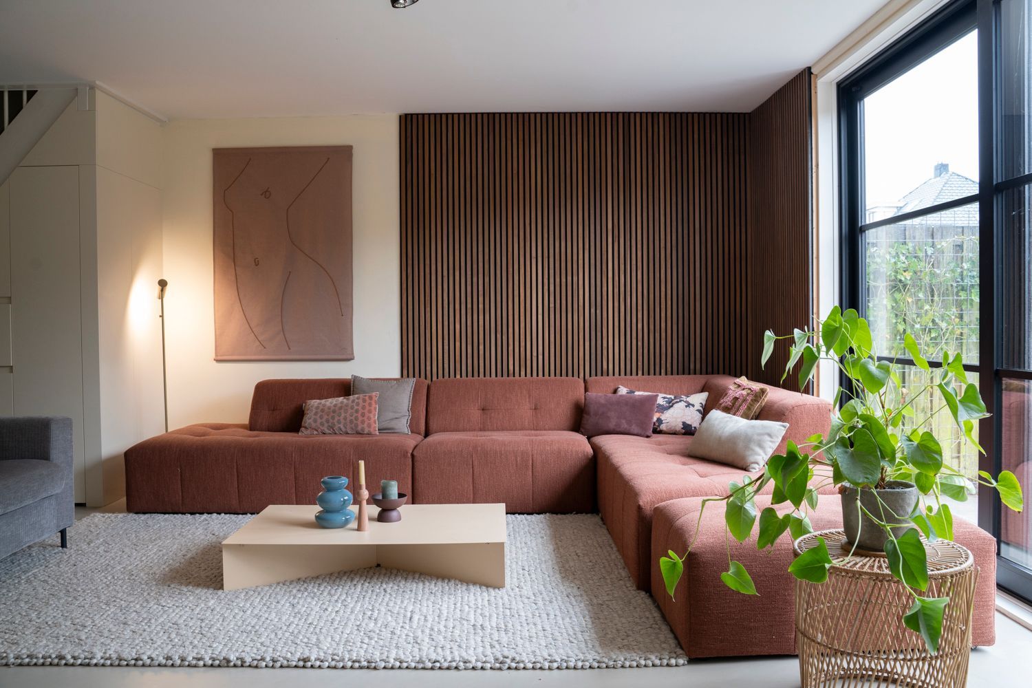 Woonkamer met een grote roodbruine hoekbank, houten wandpanelen en een groot raam.