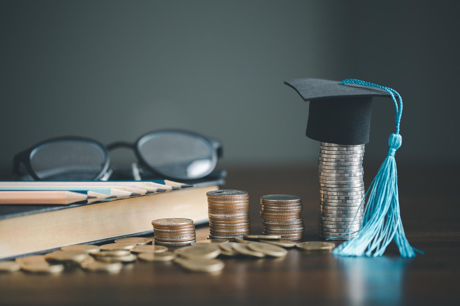 Stacks of coins with a graduation cap, glasses, pencil, and book on a table, symbolizing education funding.