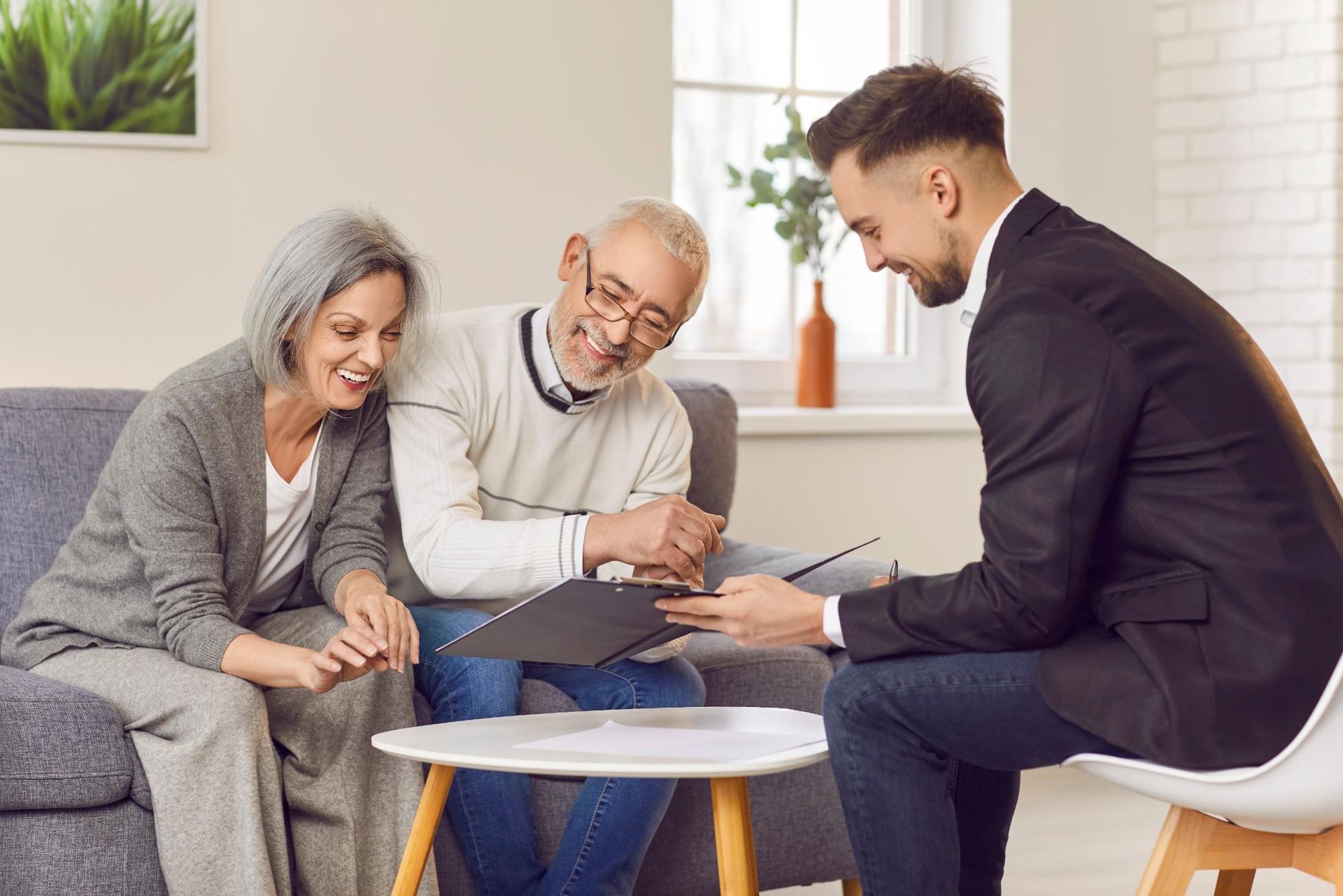 Senior couple reviews documents with a smiling financial advisor in their home.