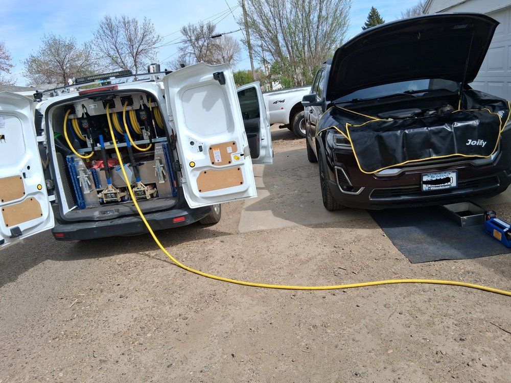 White utility van with open rear doors and equipment, parked beside a black SUV with hood open on a roadside.