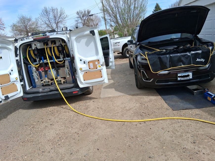 White service van with open rear doors and black SUV with open hood, connected by a yellow jumper cable outdoors