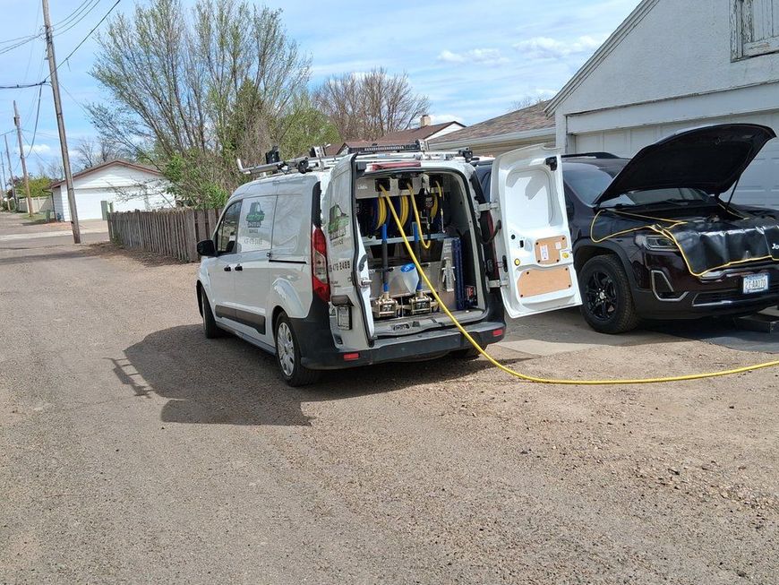 White service van with open rear doors and equipment, parked beside a black SUV with its hood open on a street.