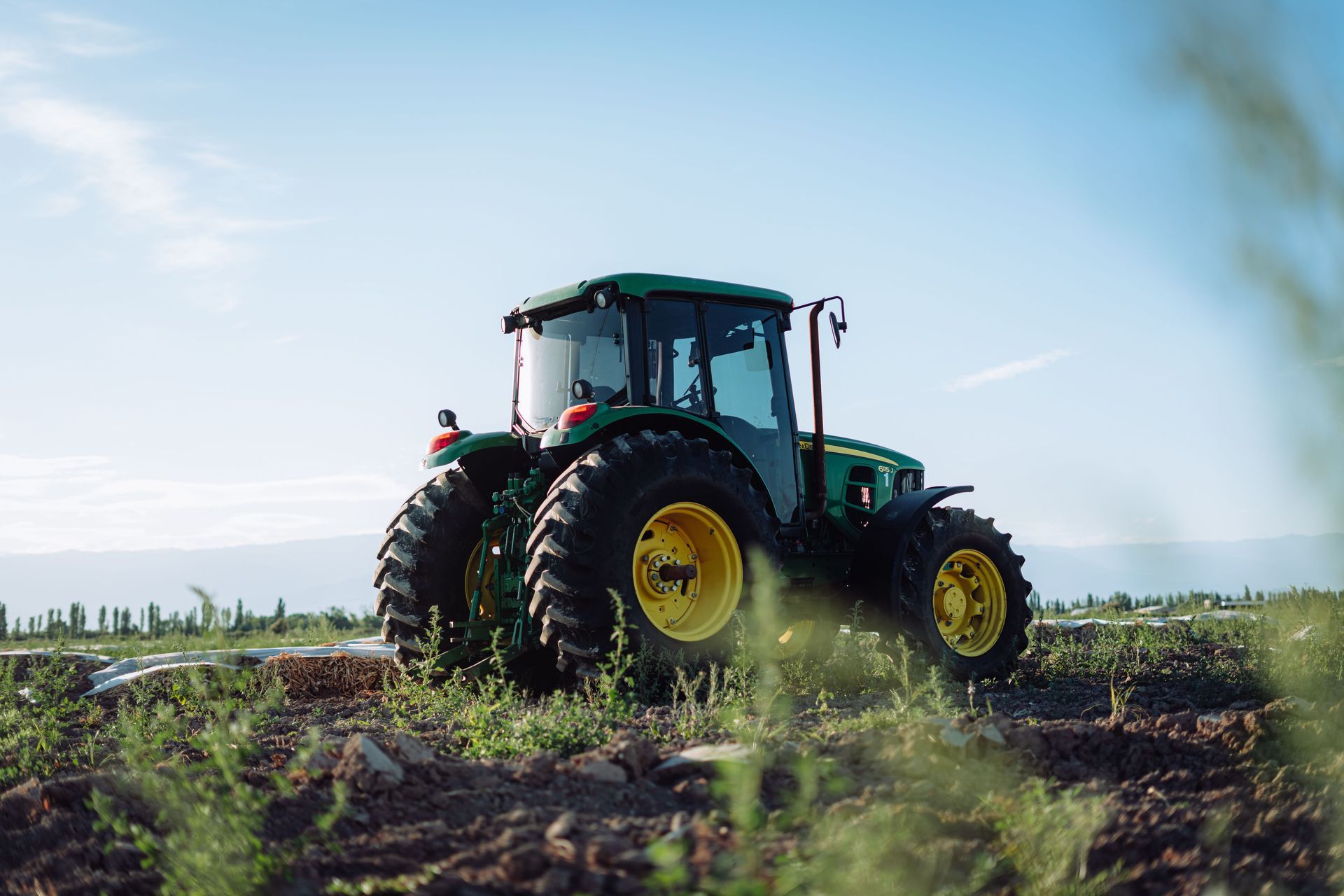 Green tractor with yellow wheels driving across a field under a blue sky