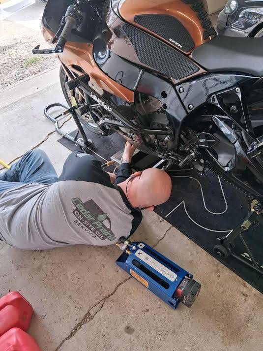 Person kneeling beside a black-and-orange motorcycle, working near the engine with a blue tool on the floor