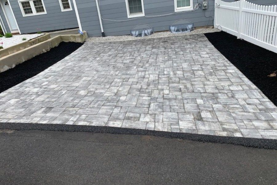 A brick driveway in front of a house with a white picket fence.
