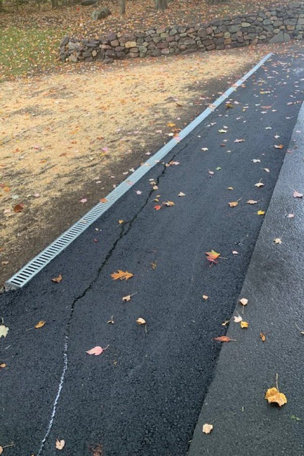 A road with a drain on the side of it and leaves on the ground.