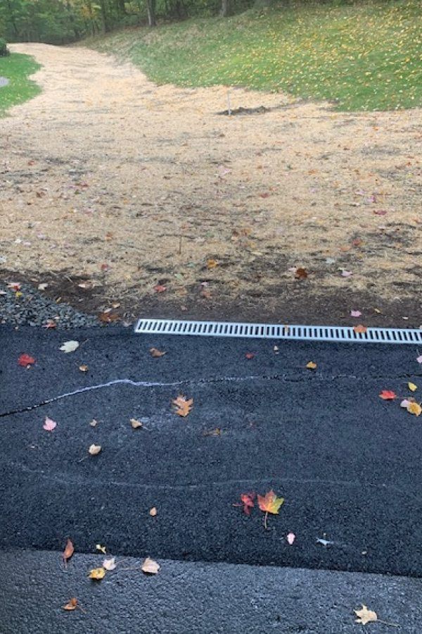A drain on the side of a road next to a dirt path.