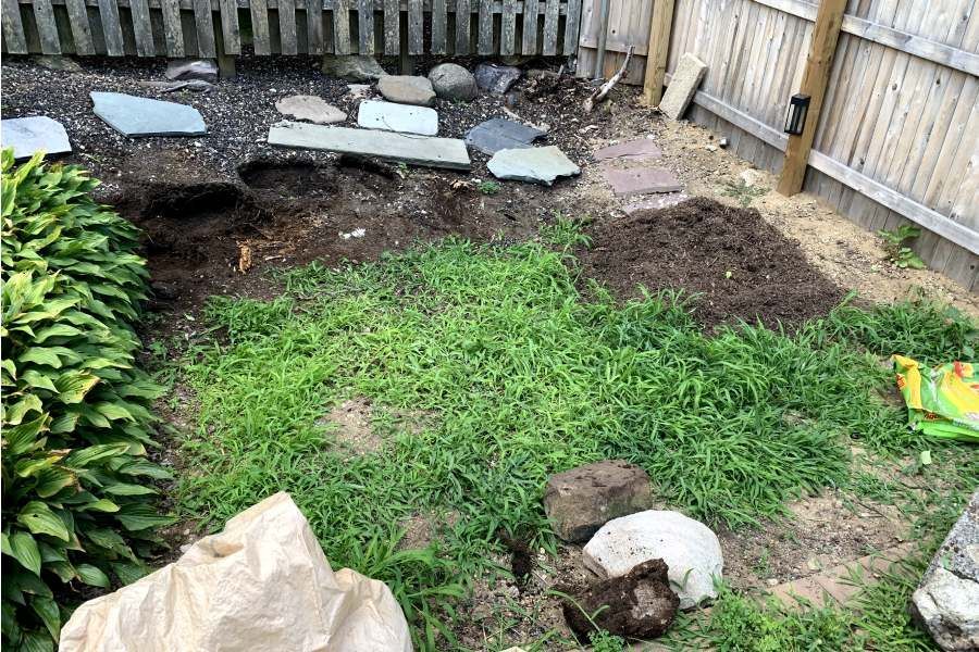A backyard with a wooden fence and a pile of dirt in the grass.