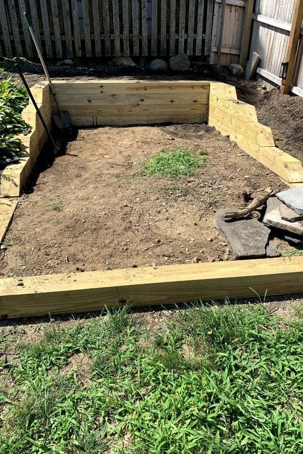 A wooden box filled with dirt and grass in a backyard.