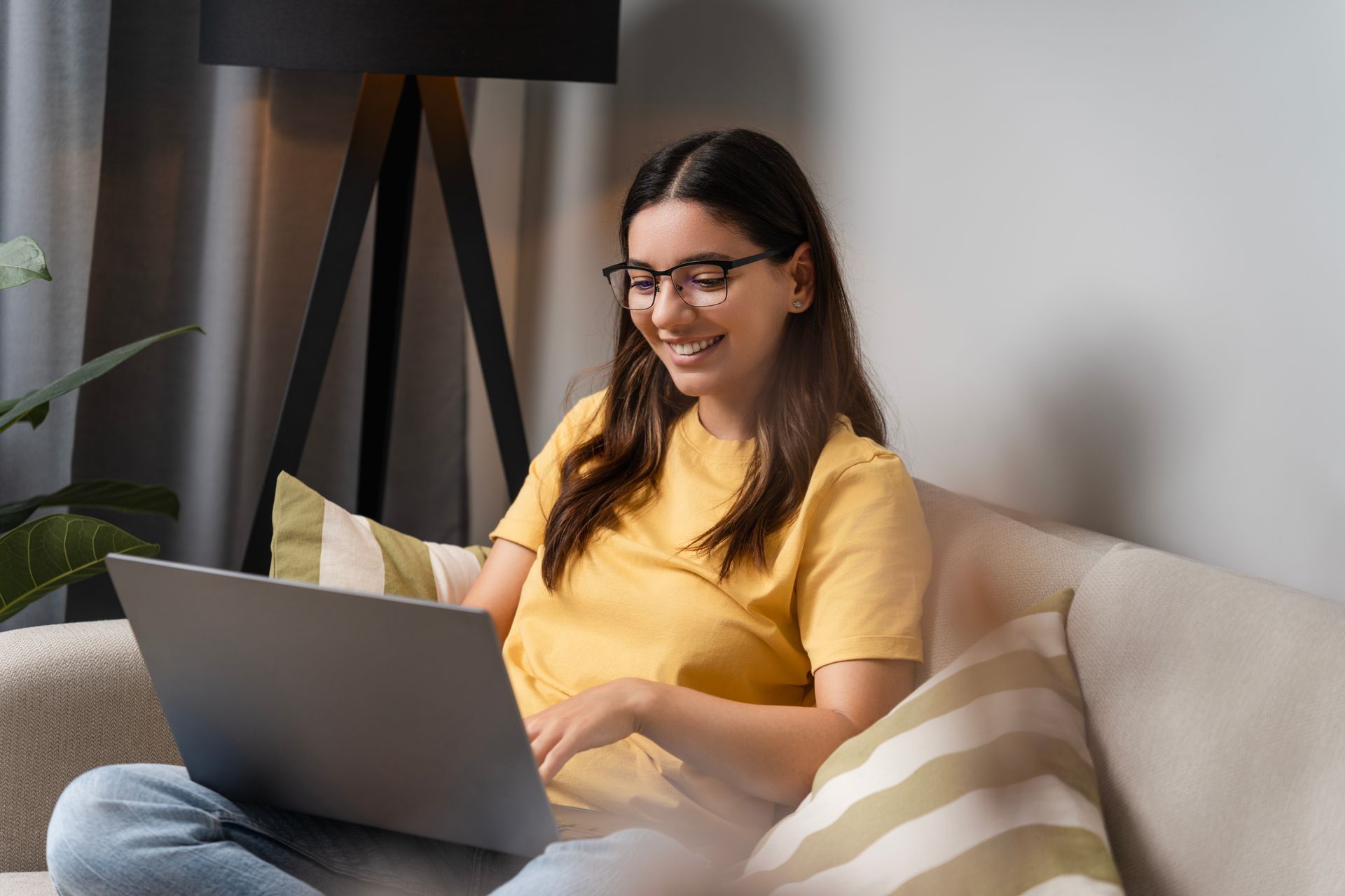 Person smiling on a couch using a laptop in a bright living room