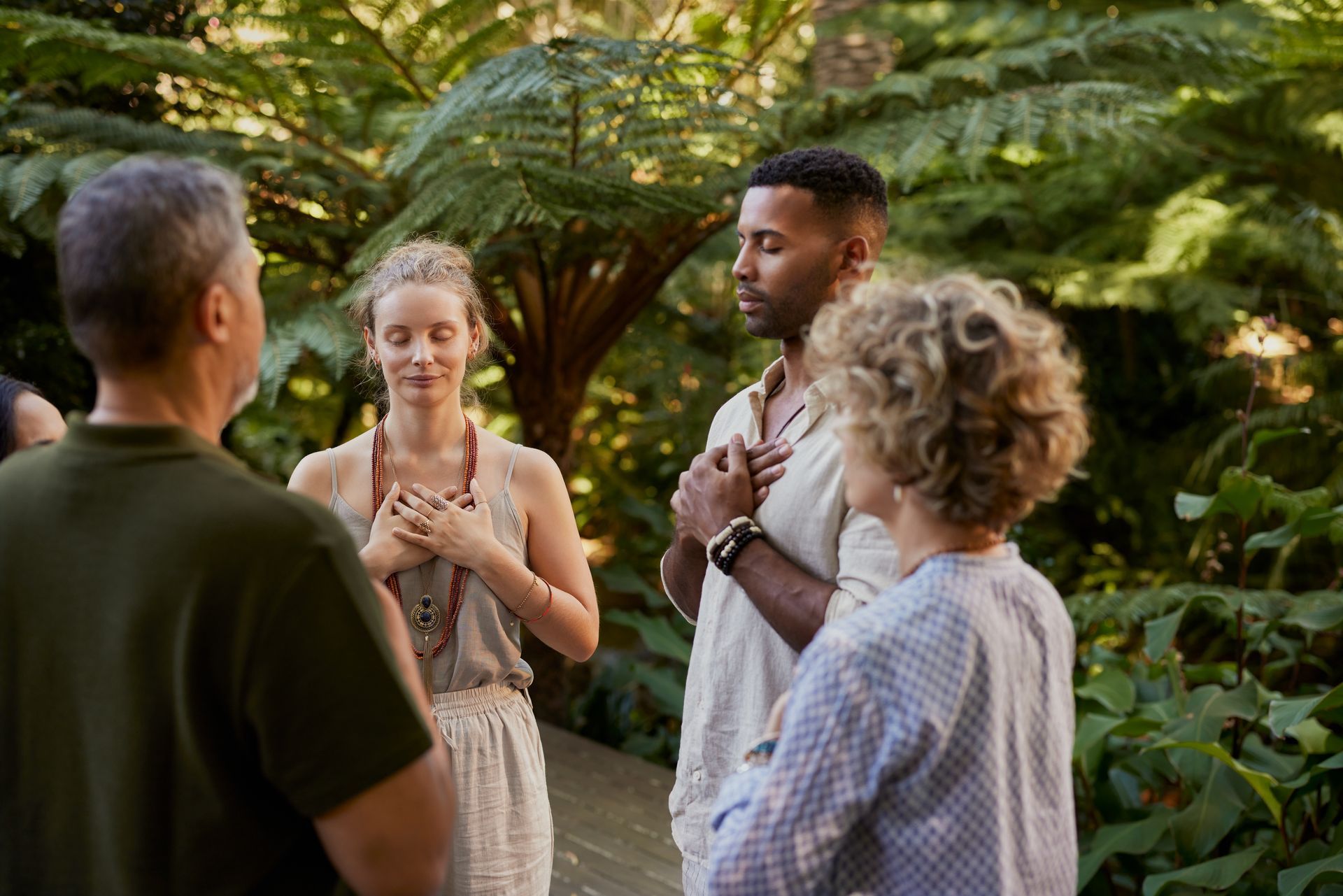 Four people stand talking in a lush garden, with hands on their chests during a calm outdoor gathering.