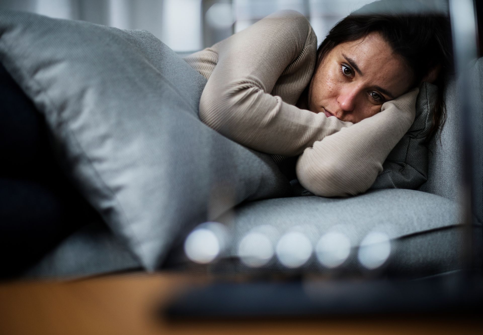 Woman lying on a couch, looking pensive and upset with her head on her arms