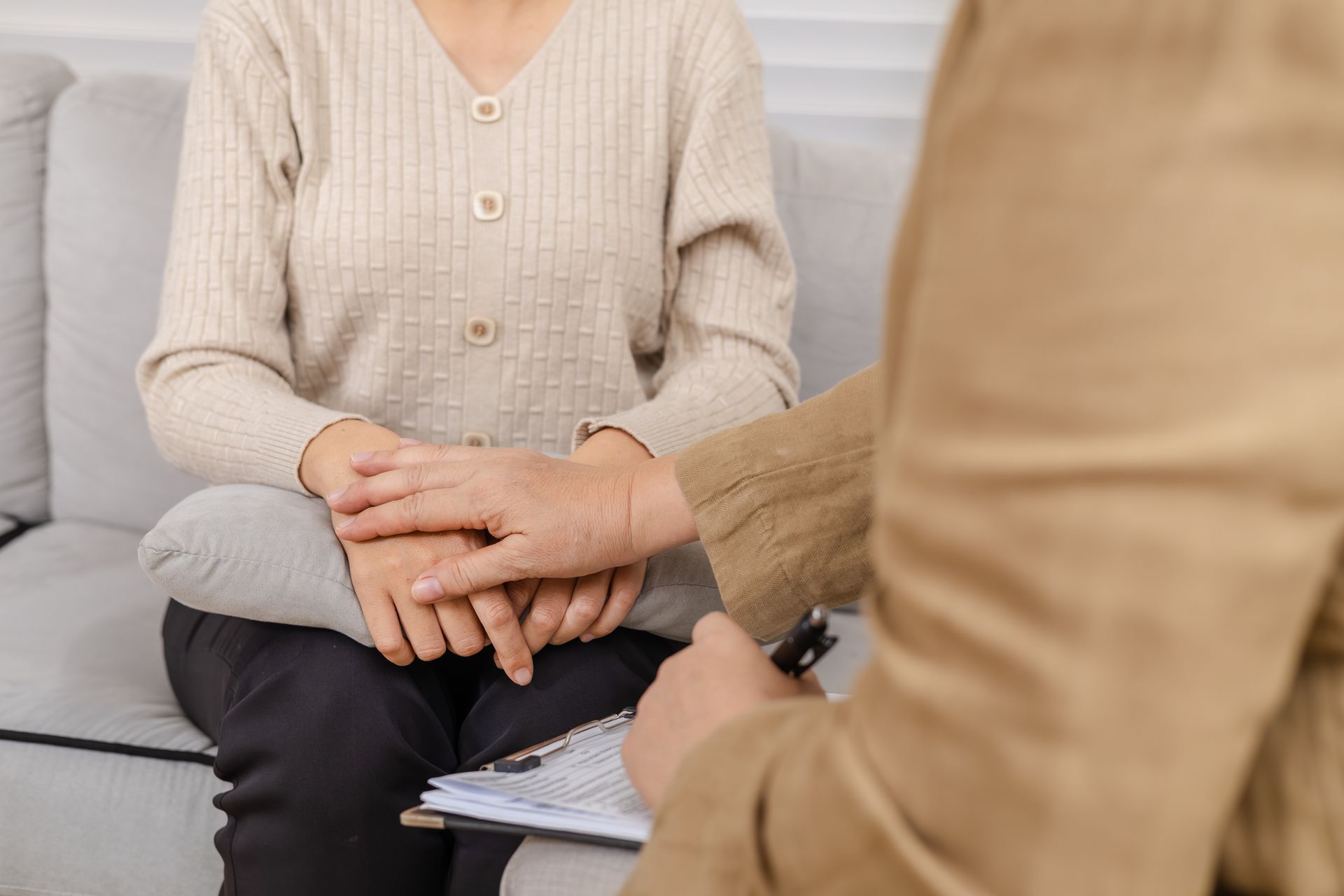 Two people seated on a couch during a 상담 session, one holding the other's hands.