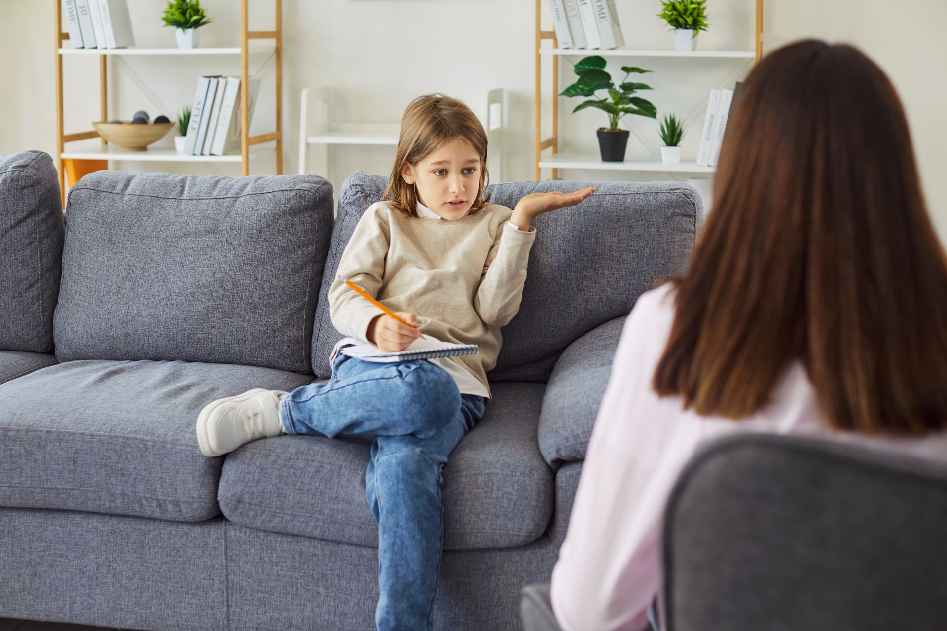 Child sitting on a gray couch talking with an adult in a bright living room
