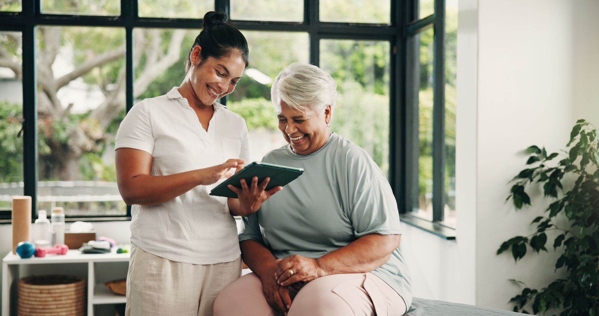 Nurse showing a tablet to a smiling patient in a bright room with large windows