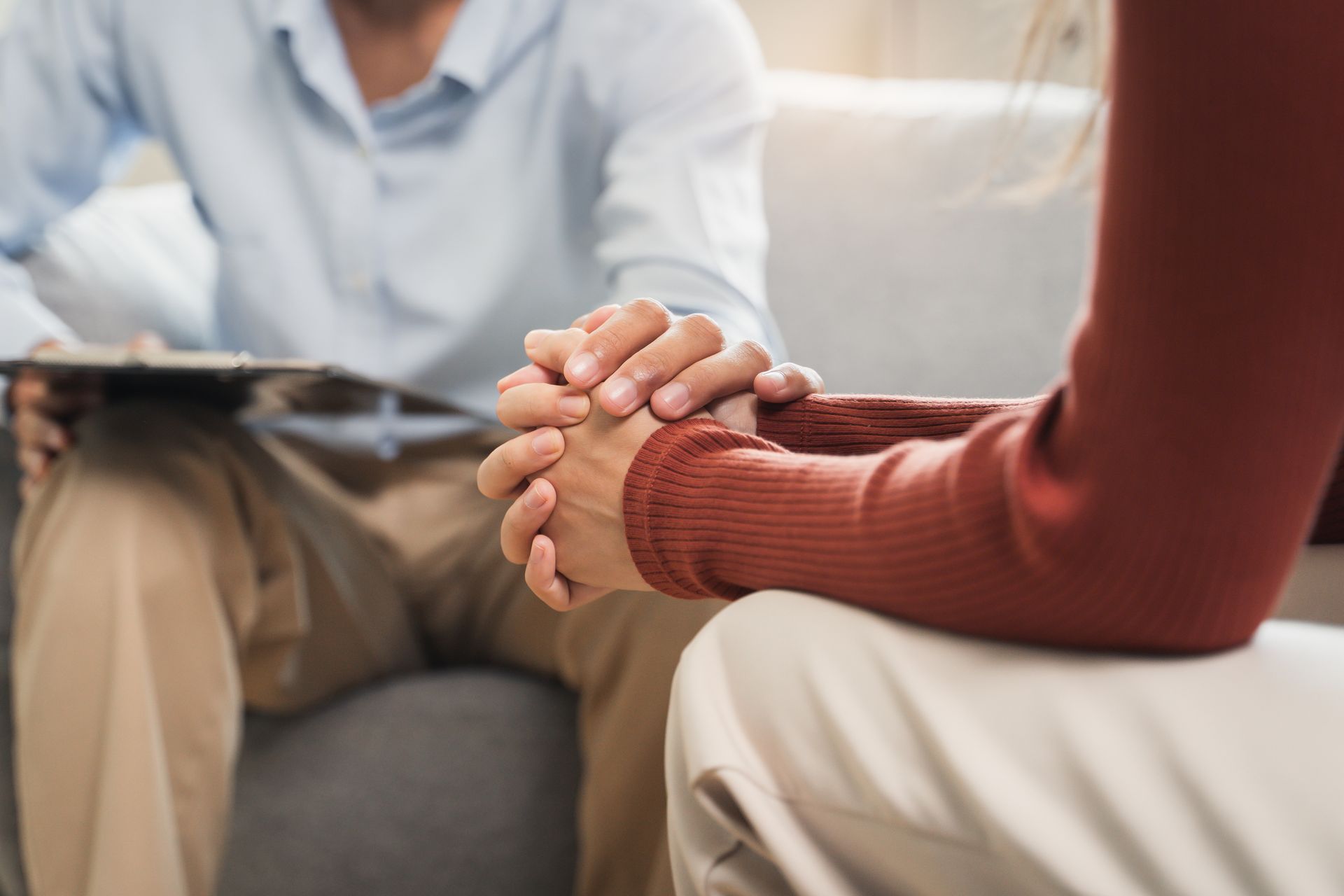 Two people sitting on a couch, holding hands in a counseling session