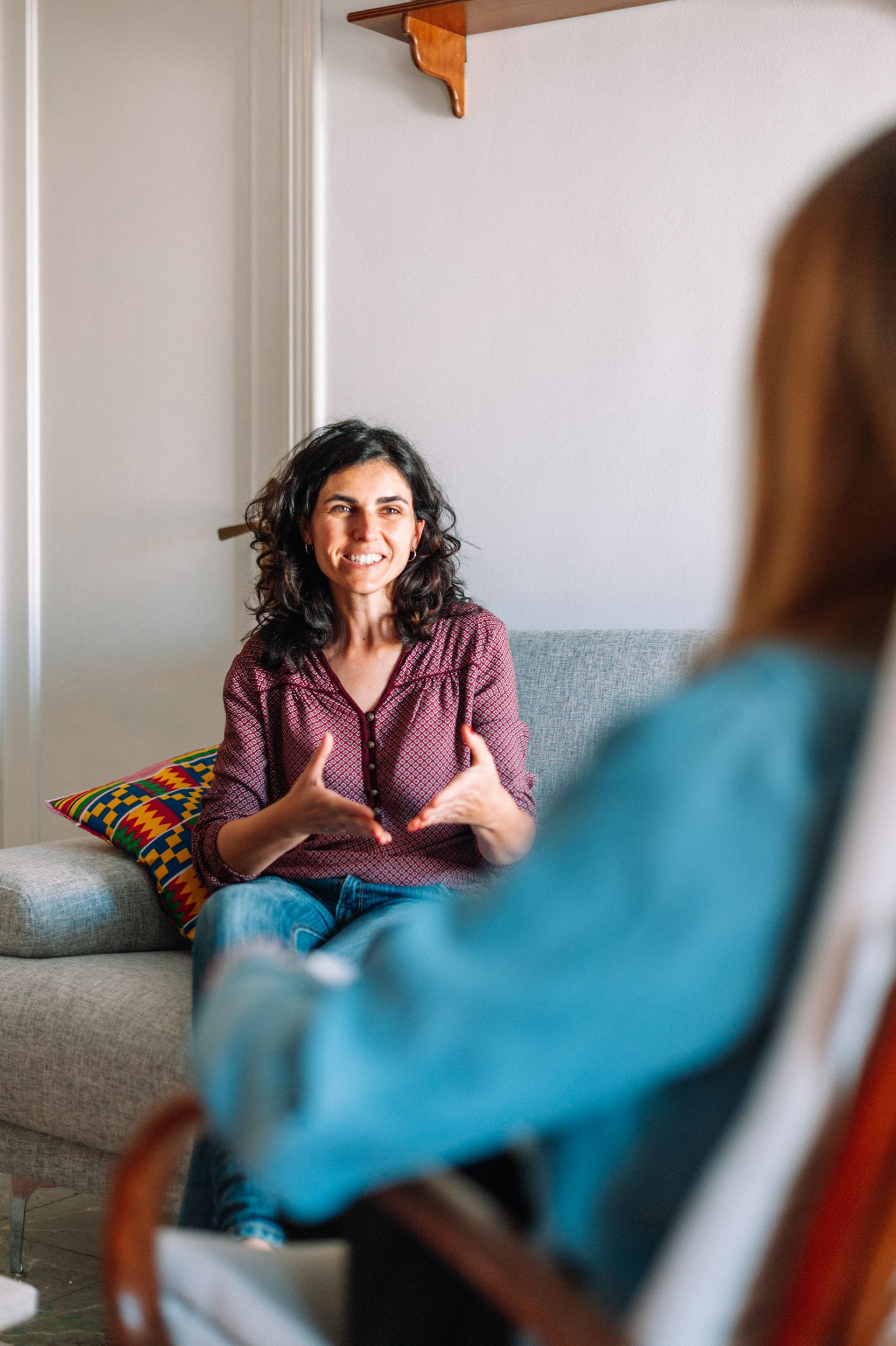 Two people in a counseling session, one seated on a sofa speaking with another in the foreground. Two people in a counseling session, one seated on a sofa speaking with another in the foreground.