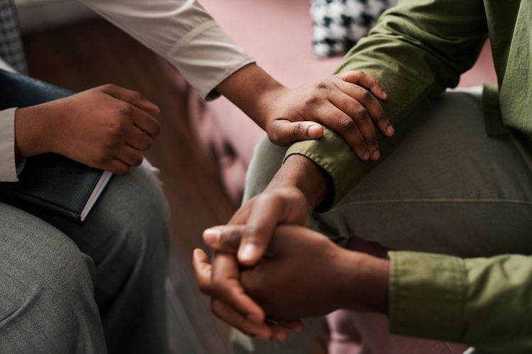People seated in a circle, hands clasped together in a supportive group meeting