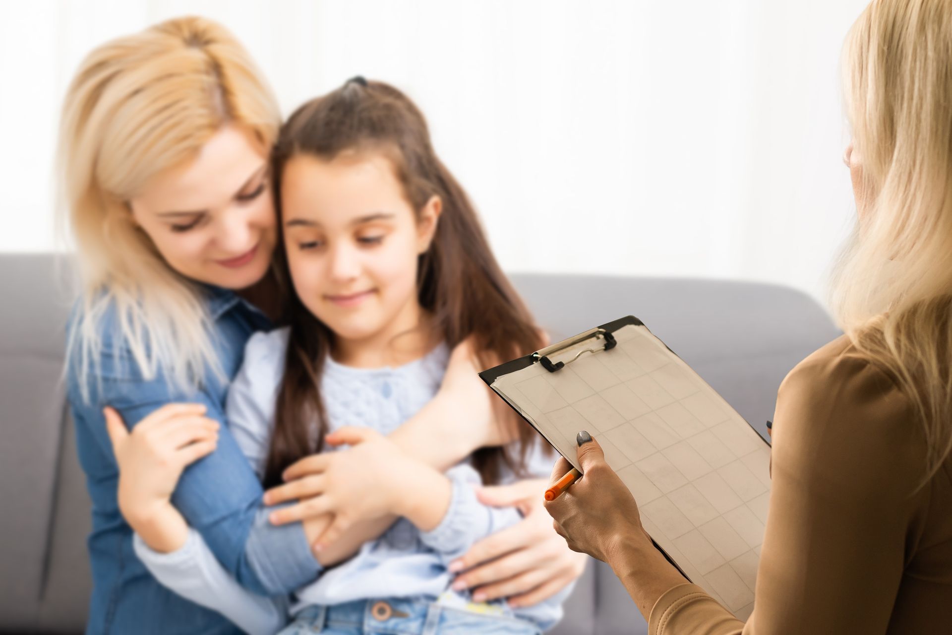 Counselor comforting a girl while taking notes during a therapy session with her mother.
