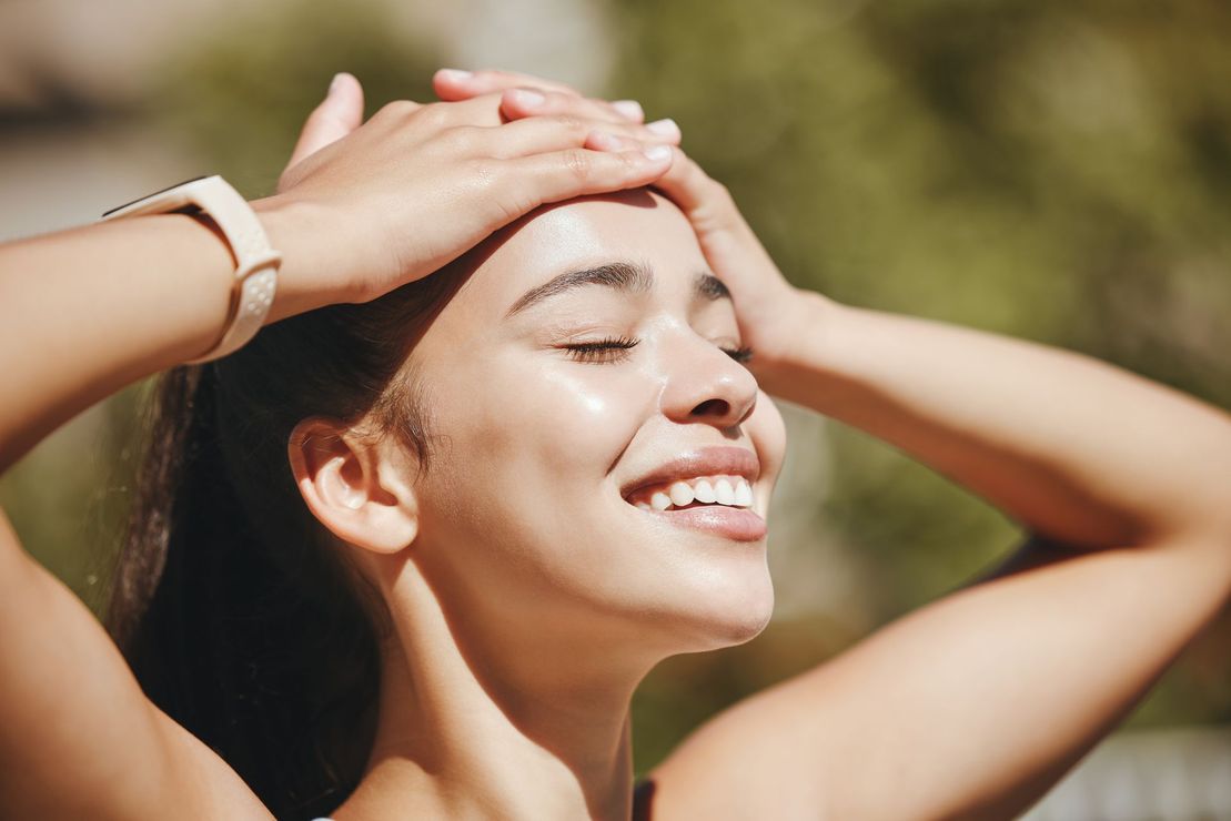 Smiling woman outdoors with hands on head in sunlight
