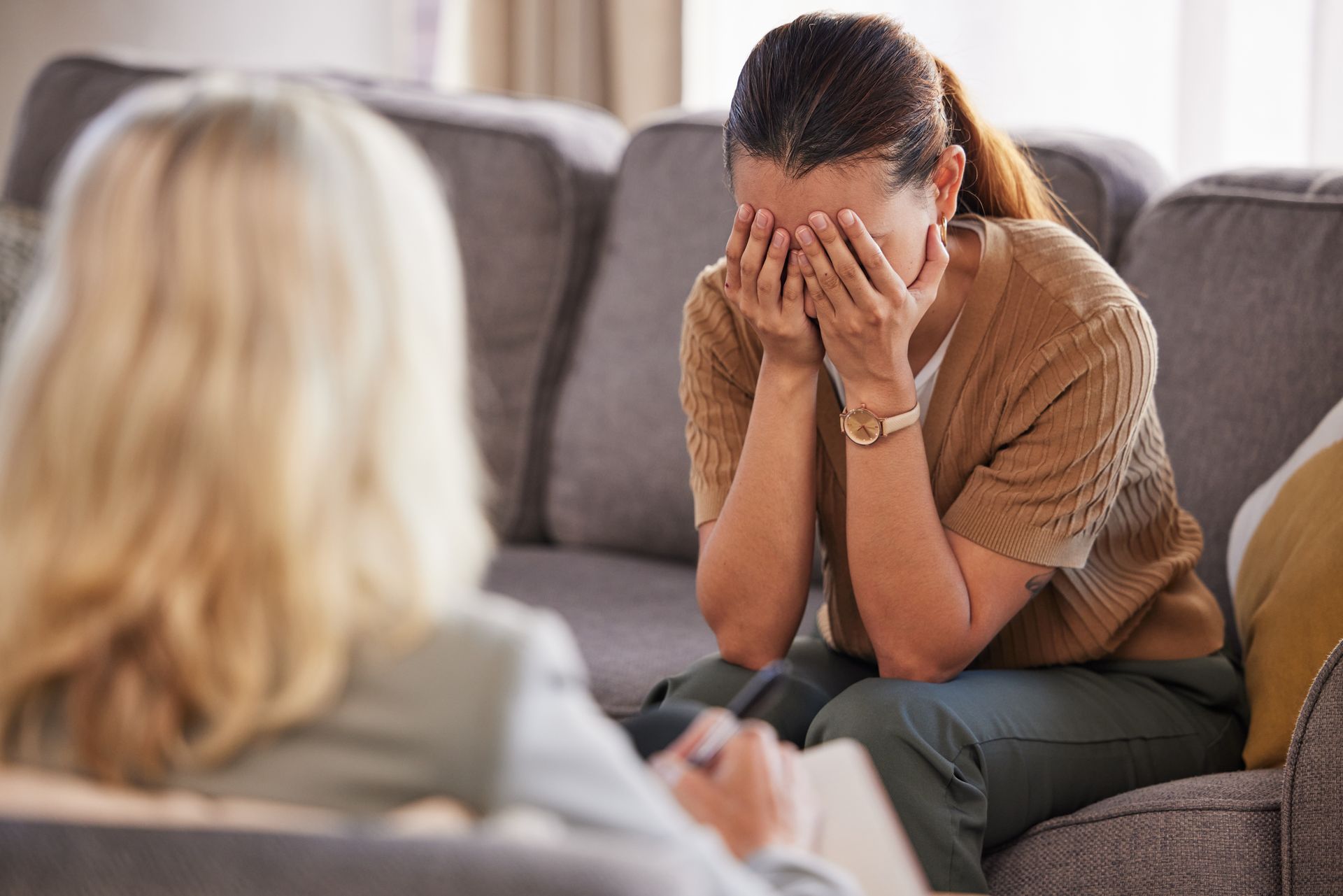Woman on a couch with her face in her hands, speaking to a blurred therapist in a counseling session