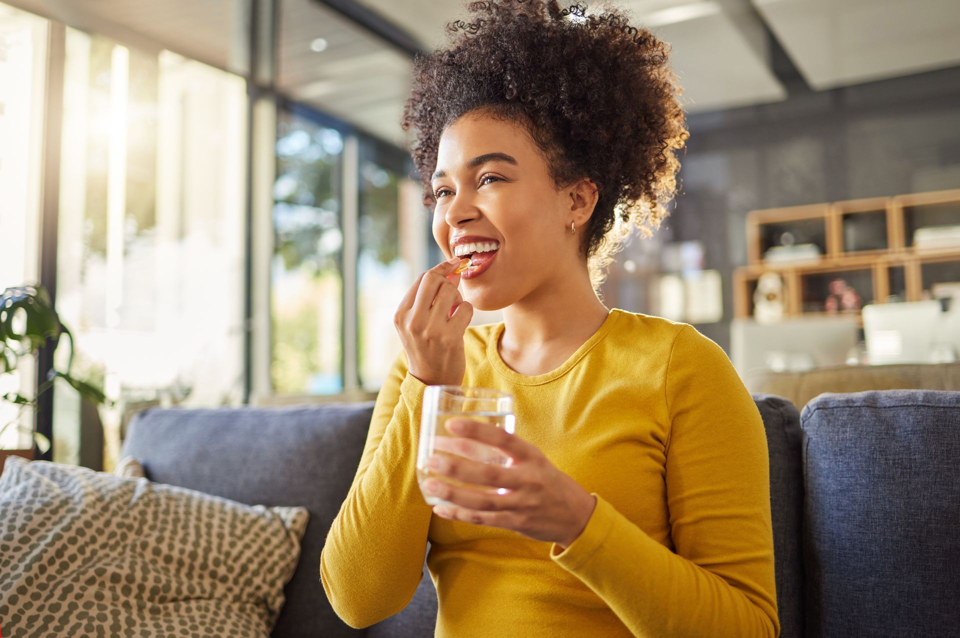 Woman in a yellow sweater eating a snack on a couch in a bright living room