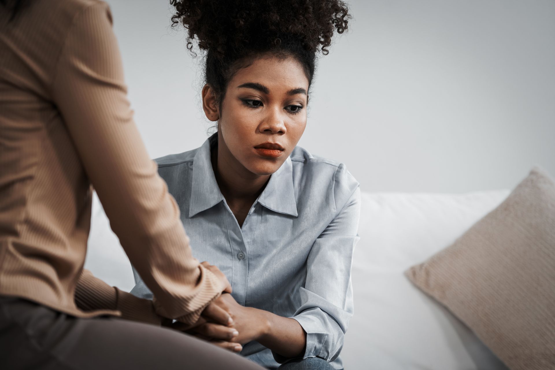 Two people sit close together on a couch, holding hands in a supportive conversation.