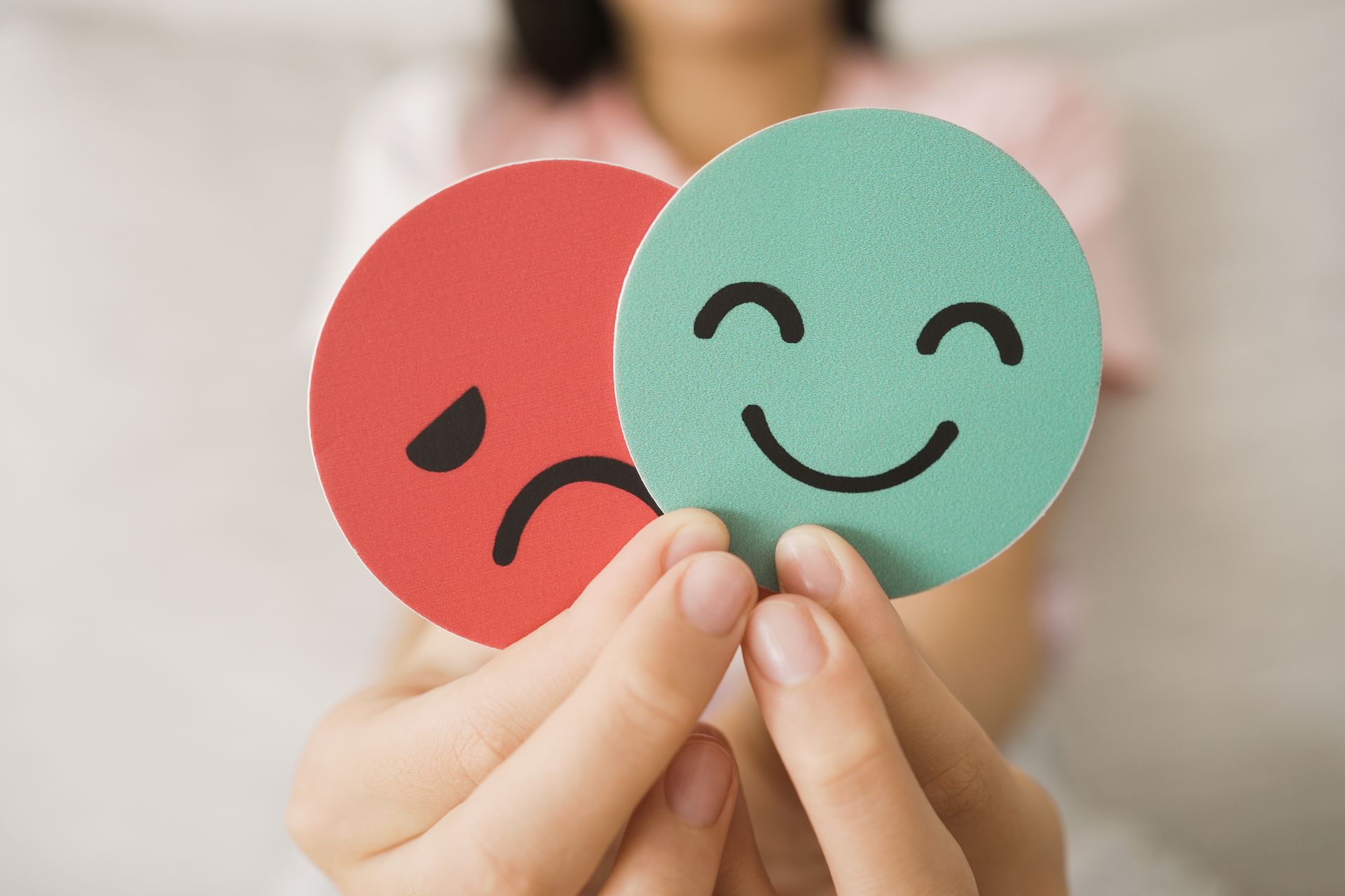 Hands holding red sad and green happy face cards against a blurred background