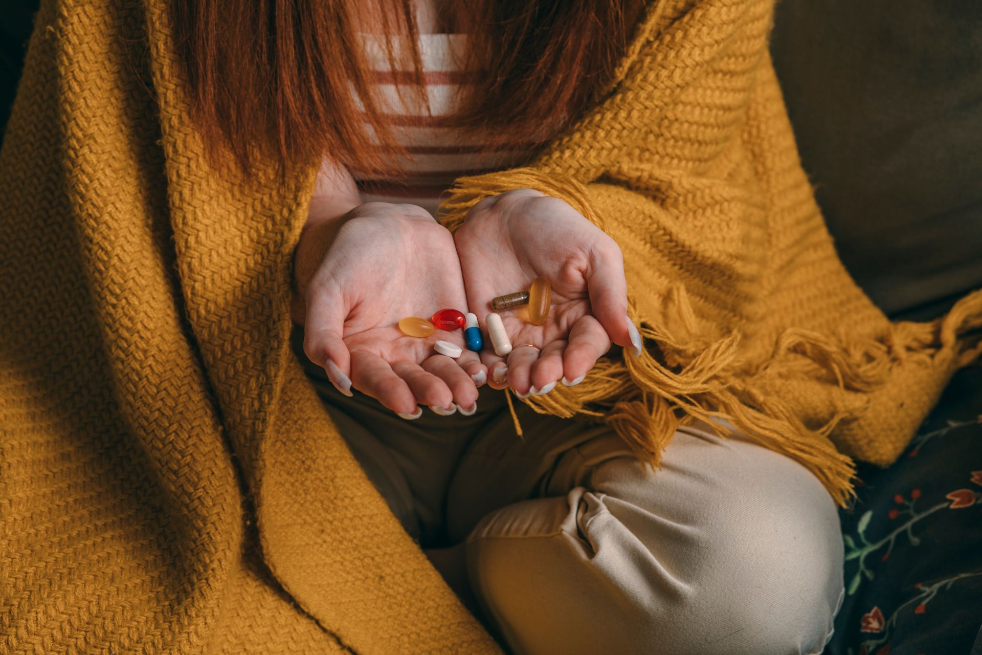 Hands holding colorful pills over a mustard knit blanket and beige pants