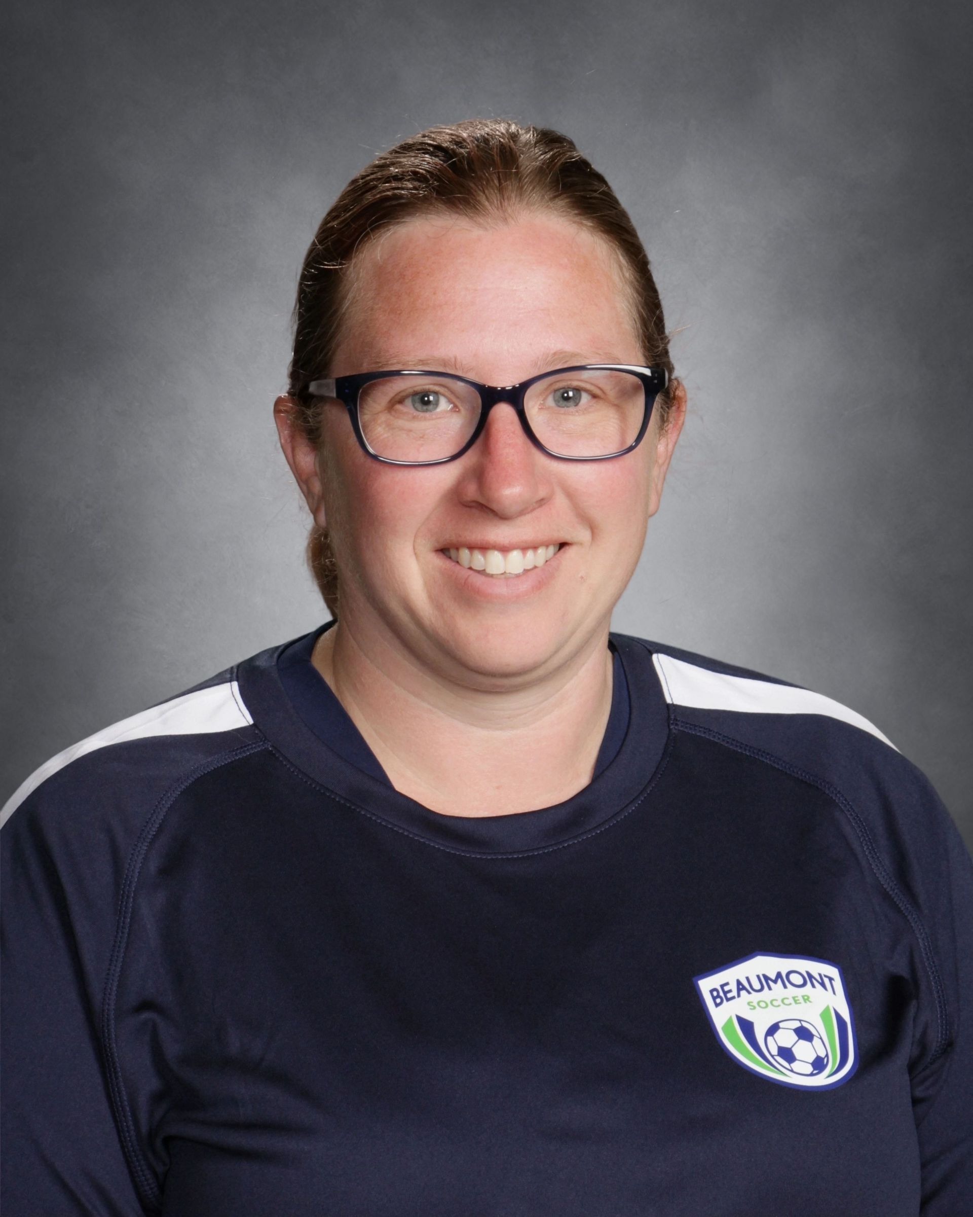 Smiling person with glasses in a blue sports jersey against a blurred outdoor background