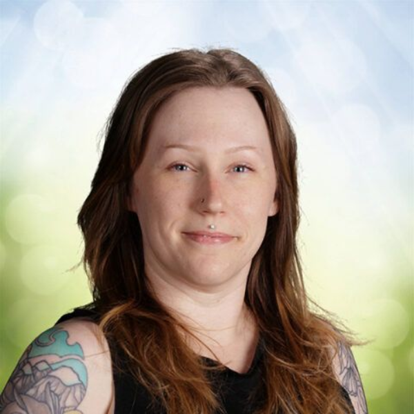 Portrait of a person with long brown hair and tattooed shoulder, against a soft green and blue blurred background
