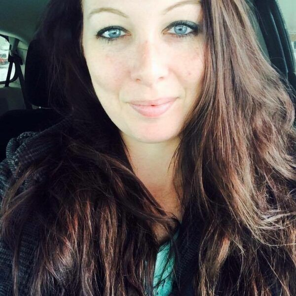 Close-up selfie of a person with long brown hair, blue eyes, and a slight smile in a car