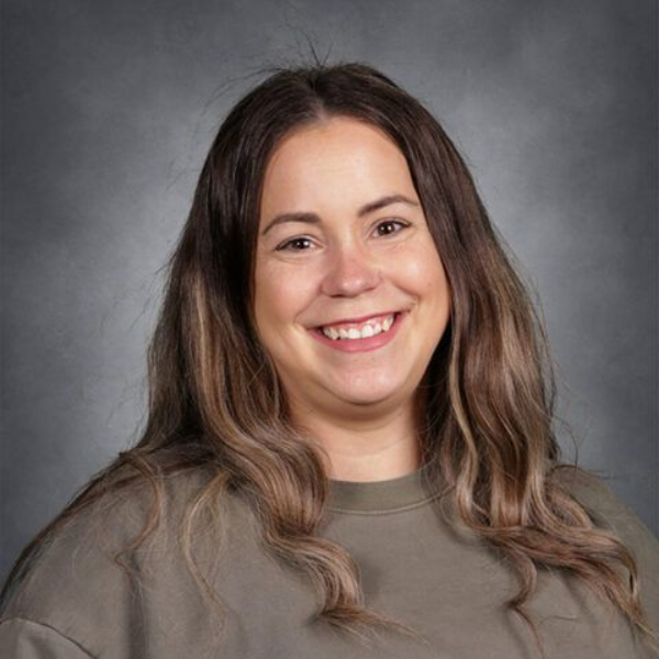 Smiling woman with long brown hair wearing a gray top against a gray studio backdrop