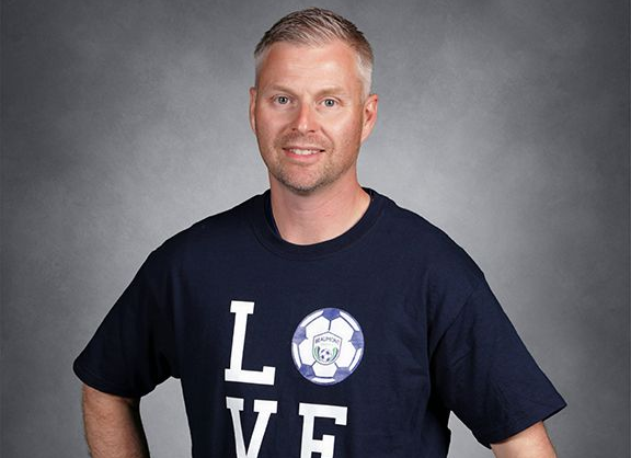 Smiling man in a navy T-shirt with large white “LOVE” letters, standing against a gray backdrop