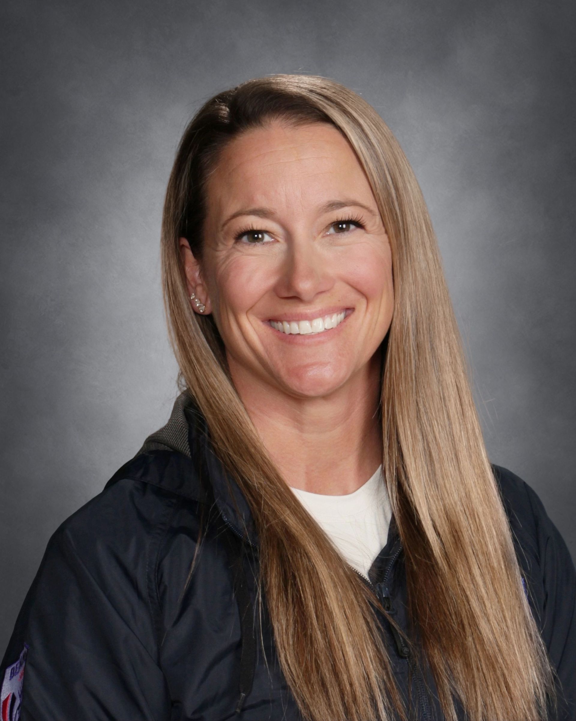 Smiling woman with straight brown hair in a navy hoodie against a soft green and blue background
