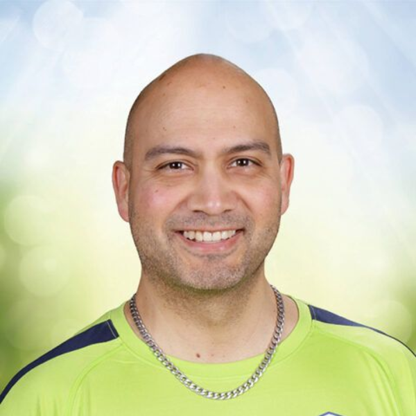 Smiling bald man in a neon green shirt and silver chain against a soft blue-green background