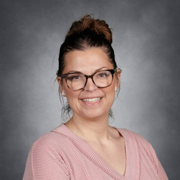 Smiling person with glasses in a pink sweater, posed against a gray backdrop