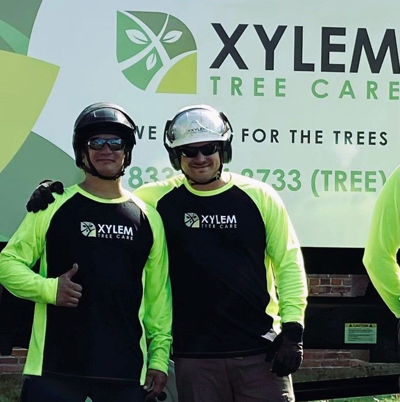 Two men are posing for a picture in front of a xylem tree care sign — Norfolk, VA — Xylem Tree Care Two men are posing for a picture in front of a xylem tree care sign — Norfolk, VA — Xylem Tree Care